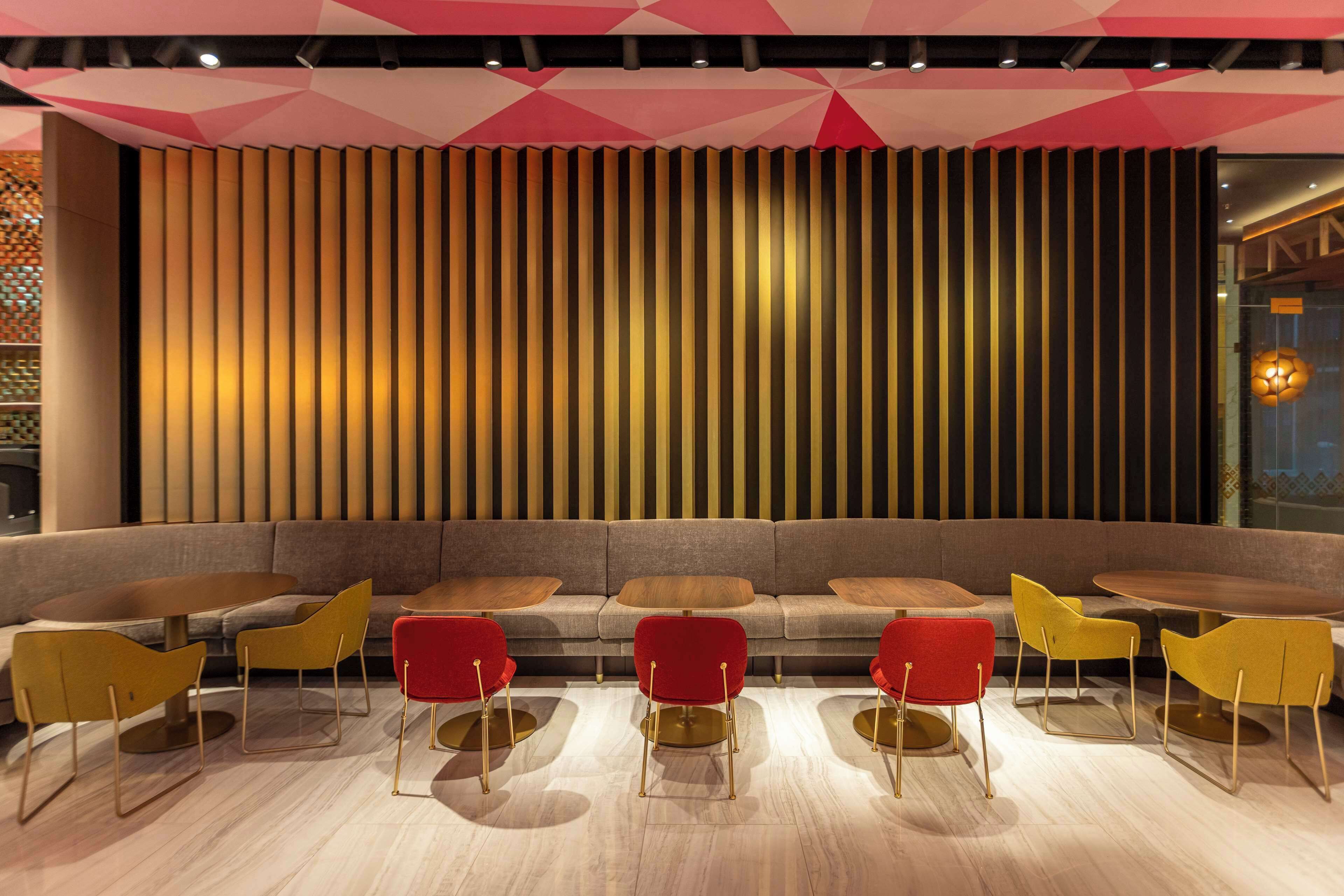 A modern interior with a sofa and chairs arranged around a central table, a patterned wall, and a geometric ceiling design.