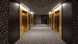En hall med mönstrat golv och väggar, utrustad med hissar och ett tak med ett geometriskt mönster.