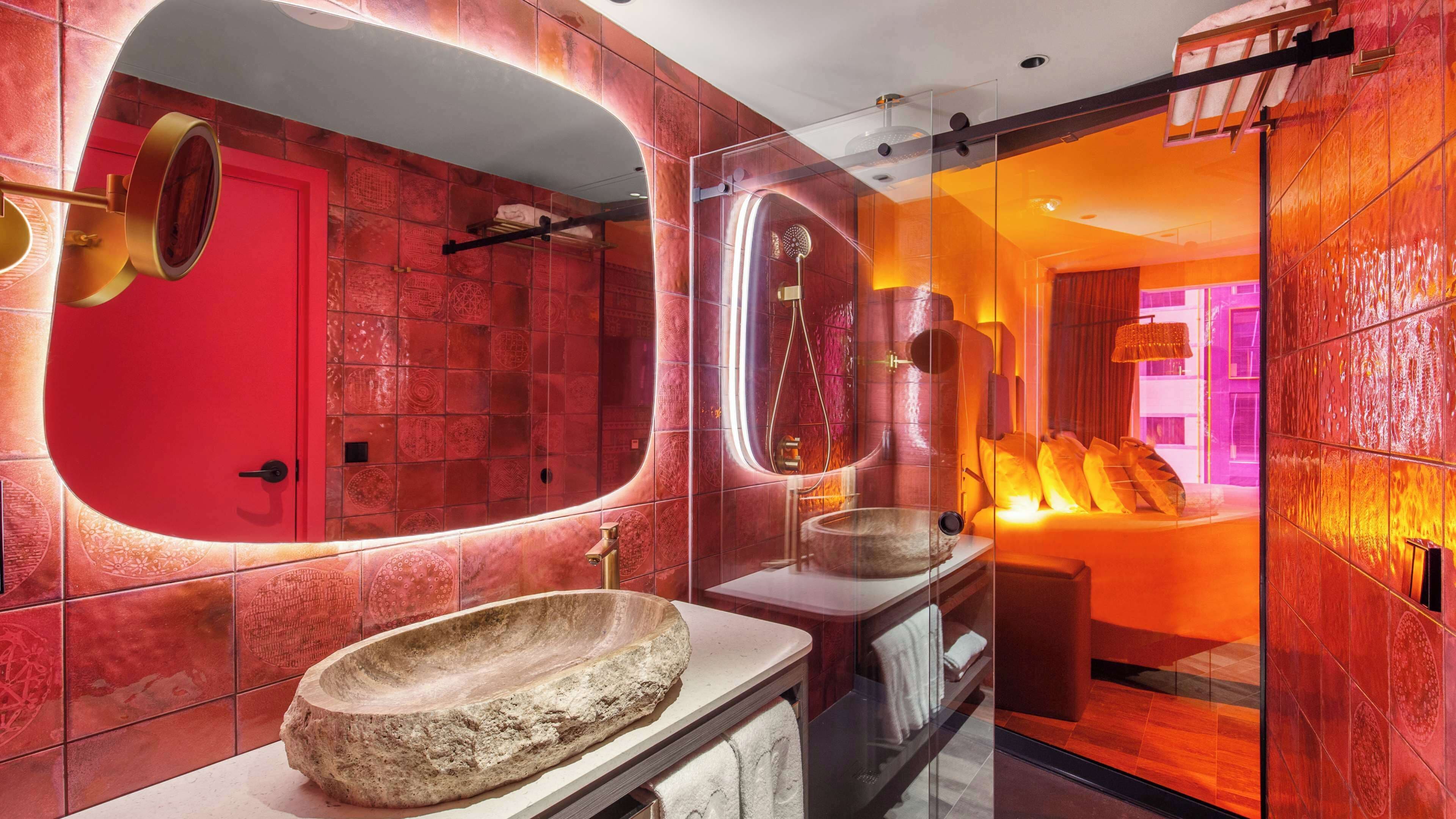 A modern bathroom with a large oval mirror, a stone basin, and a glass-enclosed shower area.