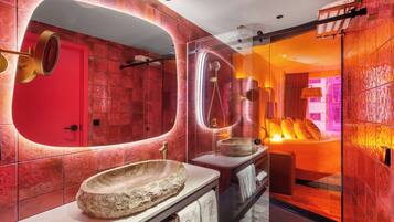 A modern bathroom with a large oval mirror, a stone basin, and a glass-enclosed shower area.