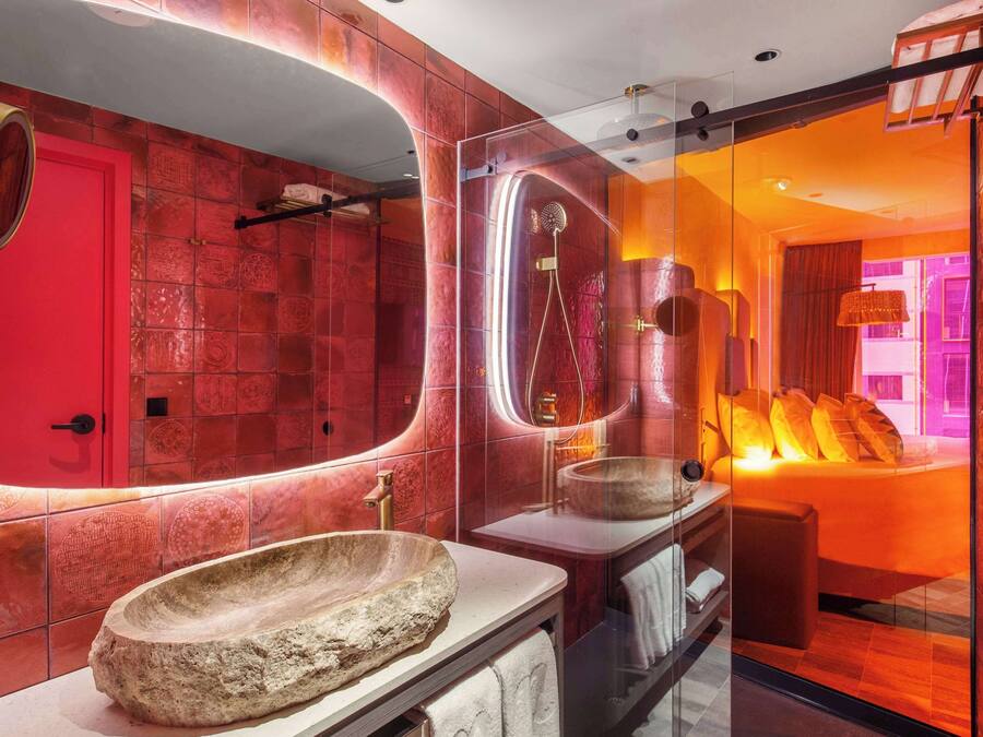 A modern bathroom with a large oval mirror, a stone basin, and a glass-enclosed shower area.