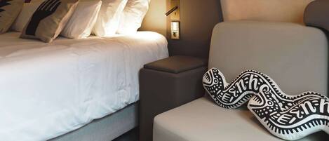 A modern bedroom with a bed, a sofa, a hanging light fixture, and a wall-mounted lamp.