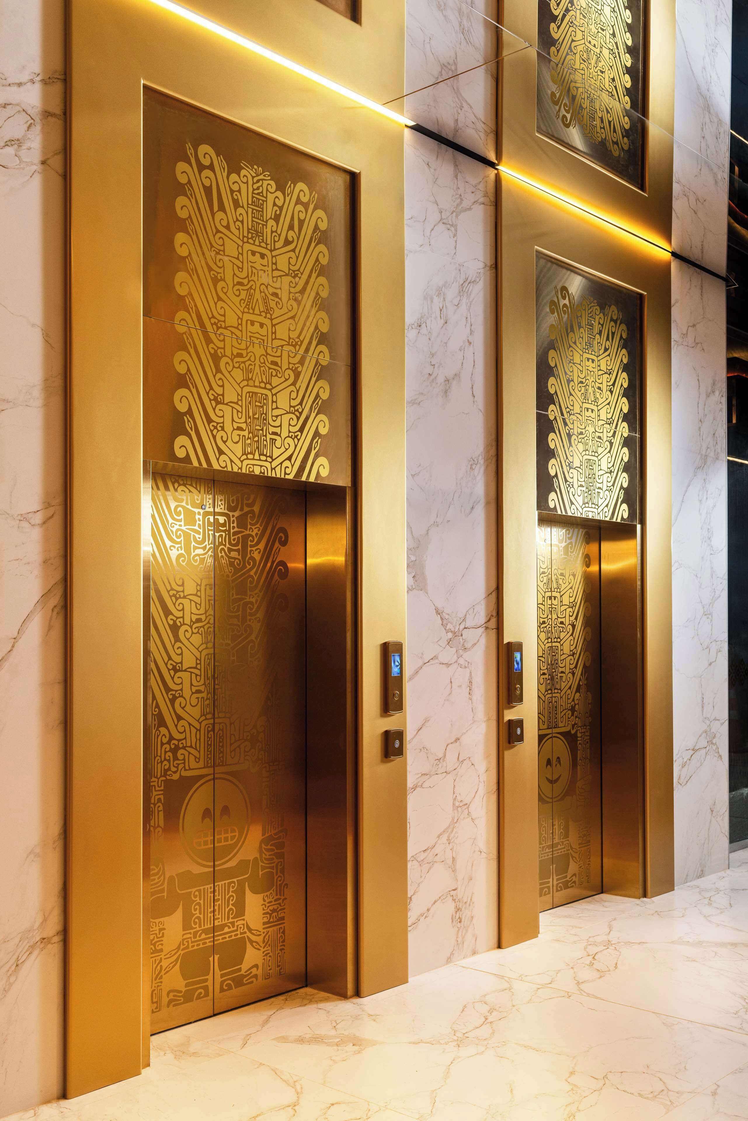 Two elevator doors with intricate golden designs and a marble floor.