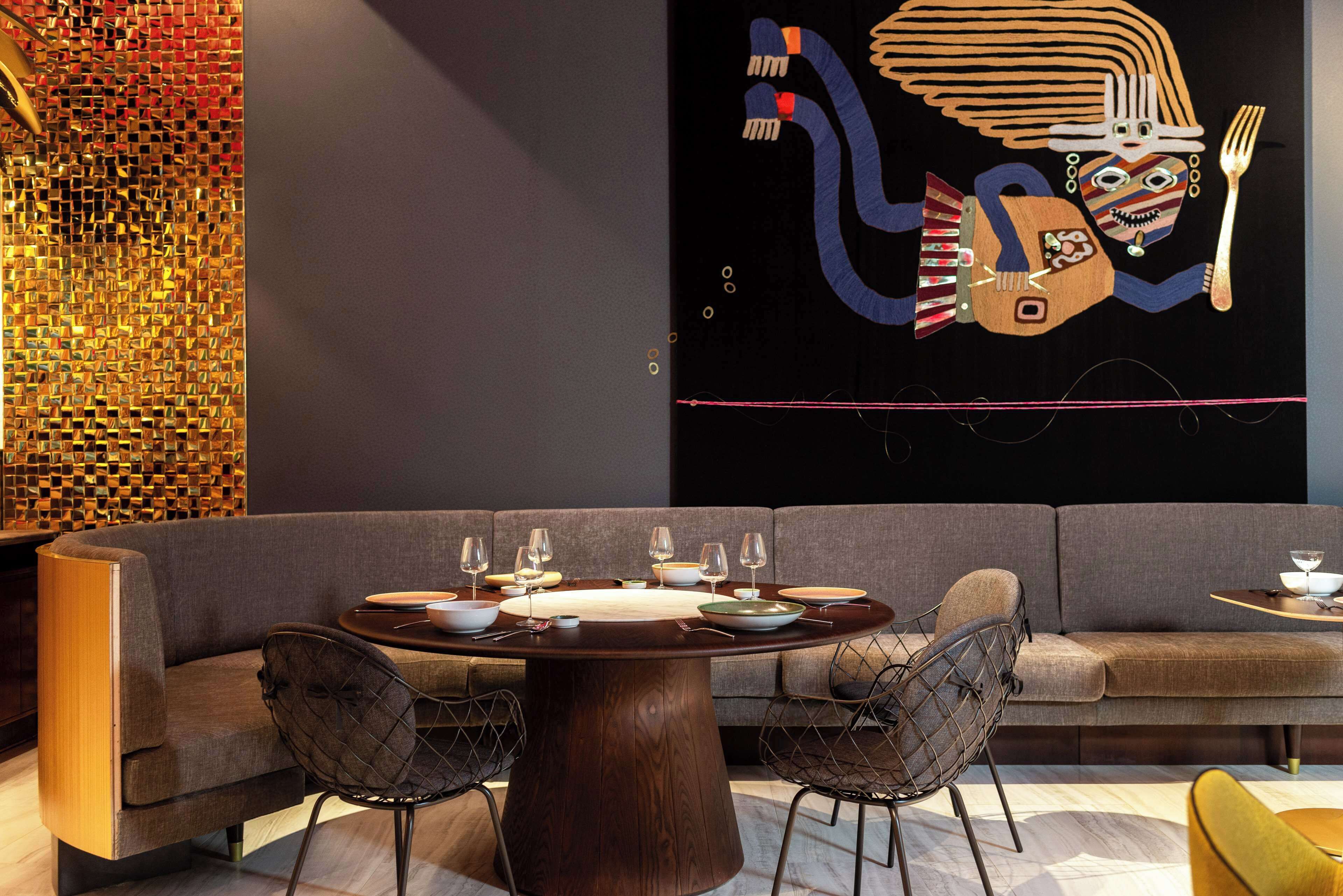 A modern dining area with a round table, grey upholstered sofa, and metal chairs.