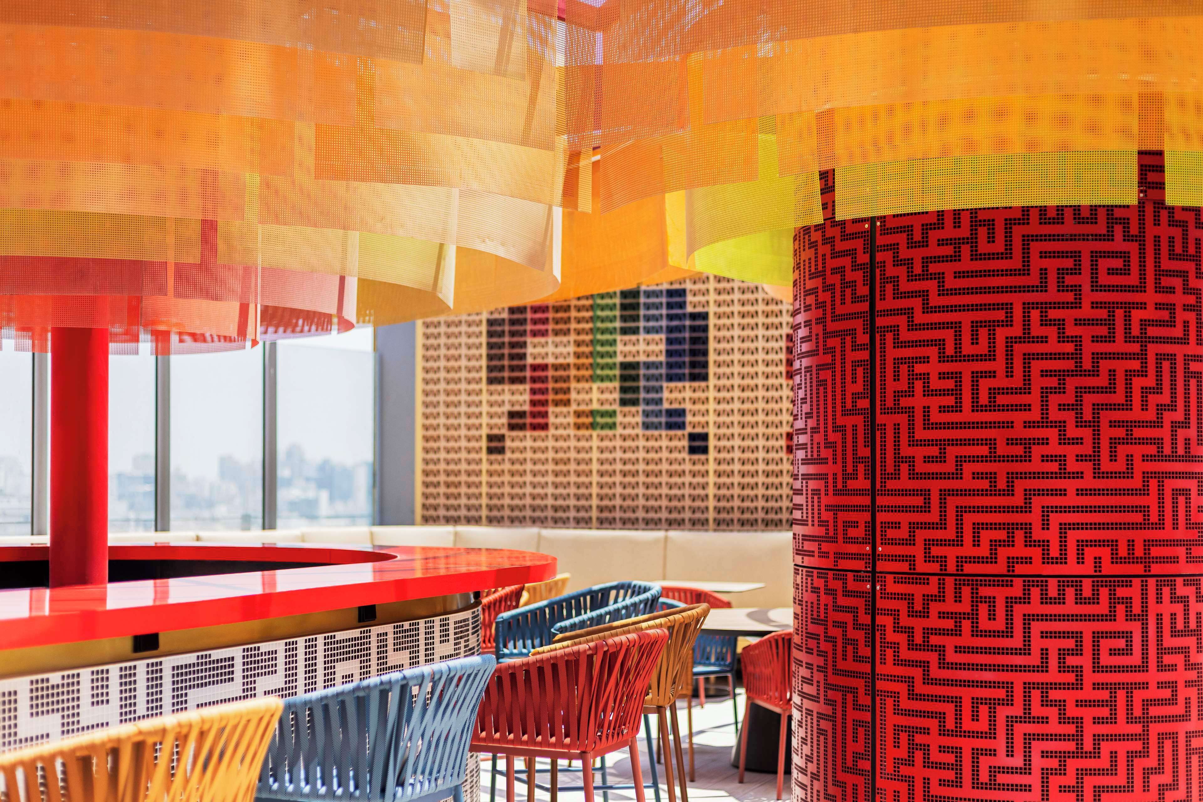 Un intérieur moderne avec une table ronde rouge, des chaises colorées et un mur orné de motifs.