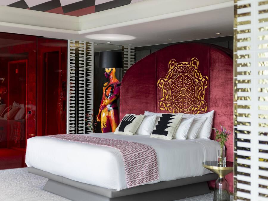 A modern bedroom with a large bed, a red accent wall, and a decorative headboard.
