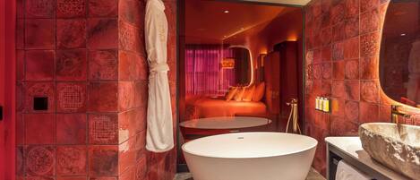 A modern bathroom with a freestanding bathtub, a round mirror, and a red-tiled wall.