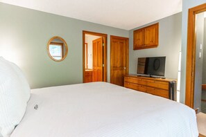 A bedroom with a large bed, a television, wooden cabinets, and a mirror.