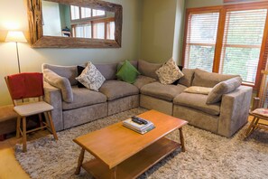 A living room with a sectional sofa, a wooden coffee table, a red chair, and a mirror on the wall.