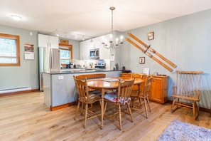 A kitchen with a central island, wooden chairs, a chandelier, and skis mounted on the wall. - Treeline 6, 3 Bedroom, 2 Bathroom Townhouse close to skiing and biking (Whistler)