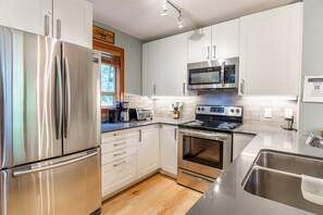 A modern kitchen with stainless steel appliances, white cabinetry, and a wooden floor.