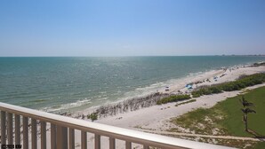 Blick auf einen Strand vom Balkon mit Geländer, dem Meer und einer fernen Küste.