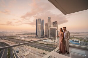 A couple on a balcony overlooking a cityscape with modern skyscrapers and a highway. - Trendy 2 Bed in Binghatti Canal (Dubai)