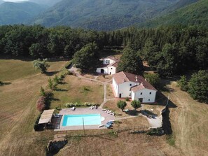 A property with a swimming pool, a white building, and surrounding greenery.