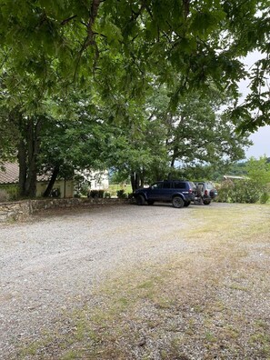 A gravel driveway leading to a parked SUV, surrounded by trees and a stone wall.