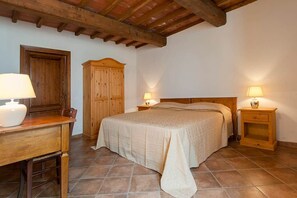 A bedroom with a bed, wooden headboard, bedside tables with lamps, a wooden wardrobe, and a desk with a lamp.