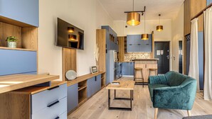 Una cocina moderna con televisor, armarios de madera y un comedor con una silla verde y una mesita.