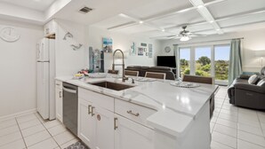 A modern kitchen with a central island, white cabinetry, and a dining area with a sofa and TV. - Easy Beach Access: First Floor Convenience (Fernandina Beach)