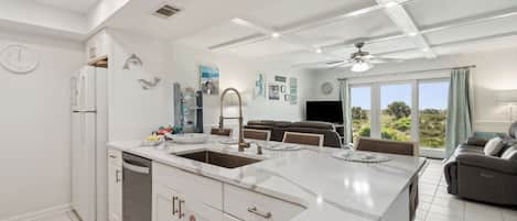 A modern kitchen with a central island, white cabinetry, and a dining area with a sofa and TV.