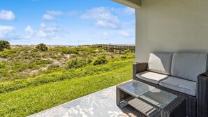 A balcony with a wicker sofa and a glass table, overlooking a beach with a wooden walkway. - Easy Beach Access: First Floor Convenience (Fernandina Beach)