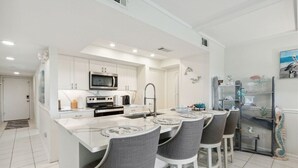 A modern kitchen with white cabinetry, a central island with bar stools, and a microwave. - Easy Beach Access: First Floor Convenience (Fernandina Beach)
