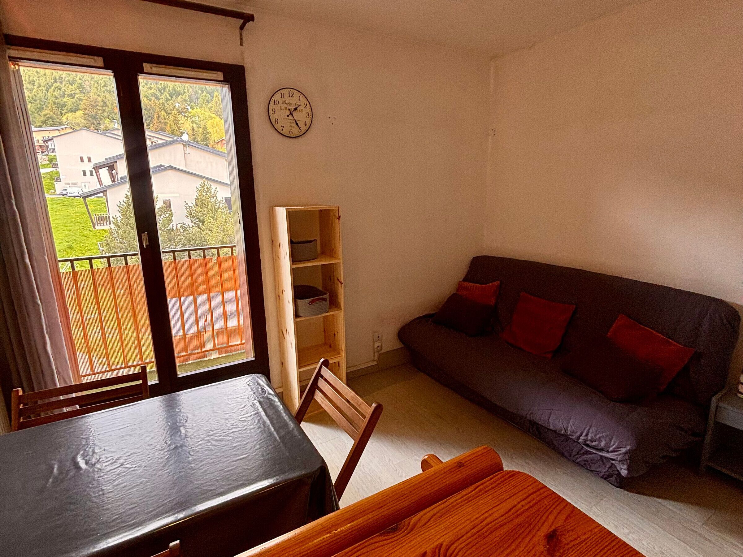 A room with a dining table, a sofa, a wooden shelf, and a clock on the wall.