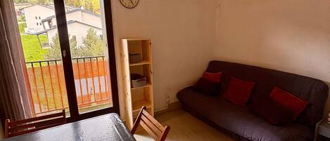 A room with a dining table, a sofa, a wooden shelf, and a clock on the wall.