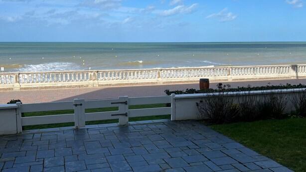 Un chemin pavé mène à une plage, avec une rambarde blanche et un banc.