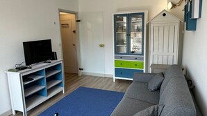Un salon avec un canapé gris, un téléviseur posé sur un meuble, un tapis bleu et un buffet blanc avec des tiroirs.