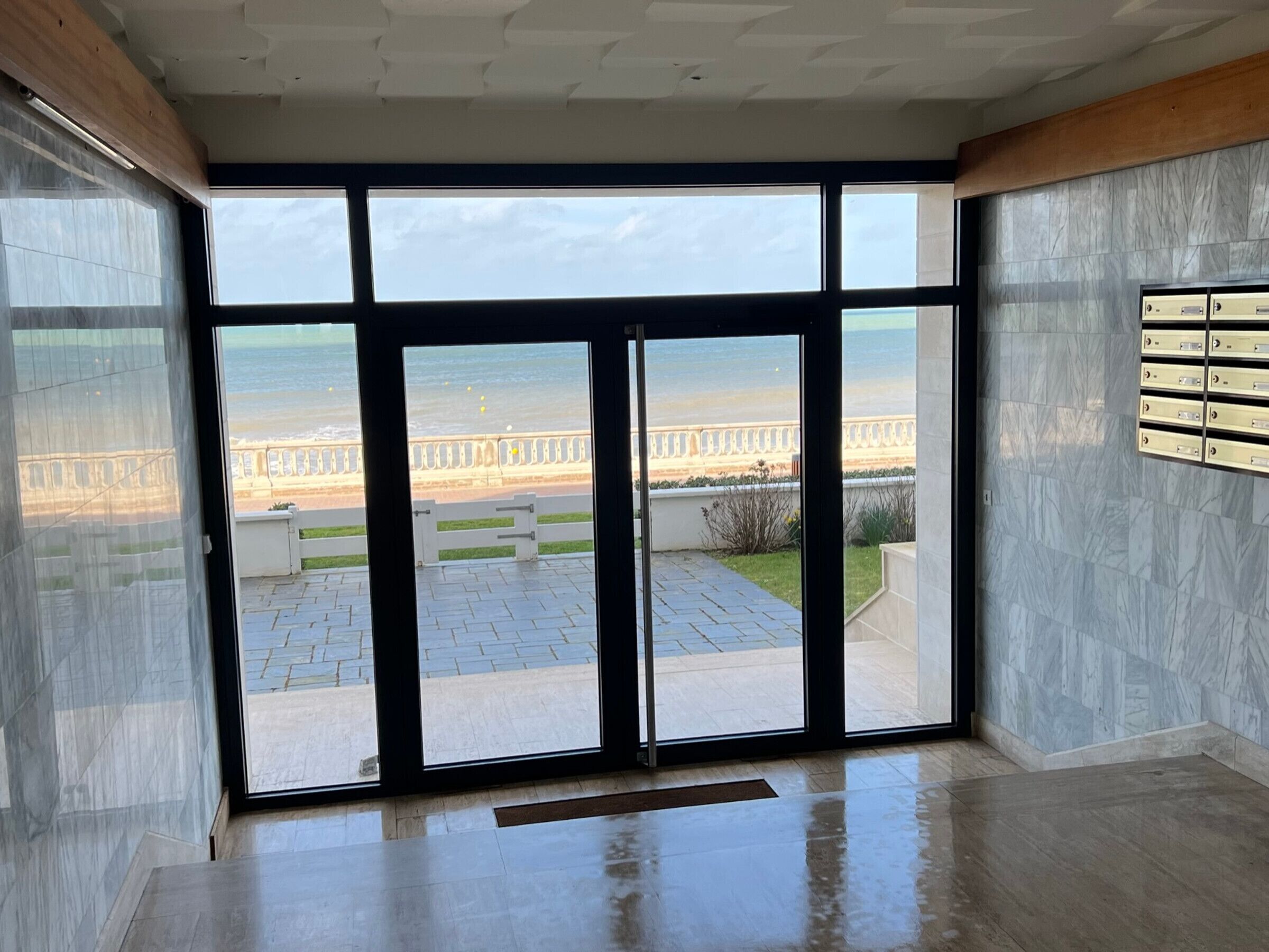 En rummelig stue med store glasdøre, der fører ud til en balkon med havudsigt og en promenade.