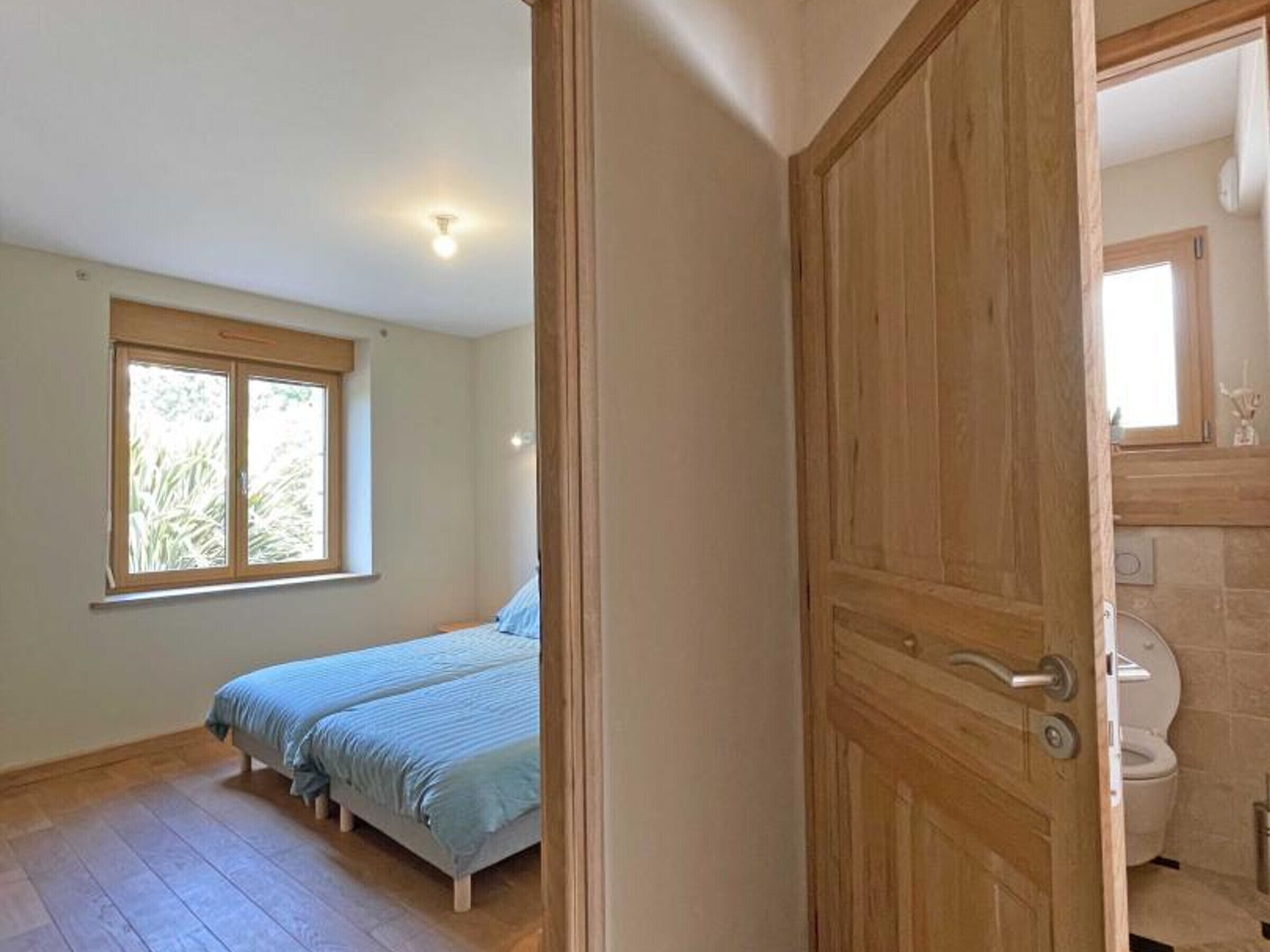 Ein Schlafzimmer mit großem Fenster, einem Bett und einer Holztür zum Badezimmer.