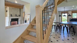 A modern kitchen with a built-in stove, a dining area with bar stools, and a staircase with wooden railings. - Country House with Garden and Spa for 14 in Les Ventes-de-Bourse (Les Ventes-de-Bourse)