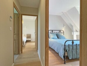 Um quarto com uma cama, piso de madeira e uma porta que dá para outro cômodo.