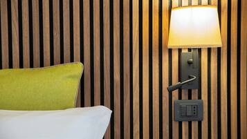 Una cama con un almohadón verde frente a una pared de listones de madera, una lámpara de pared y un enchufe.