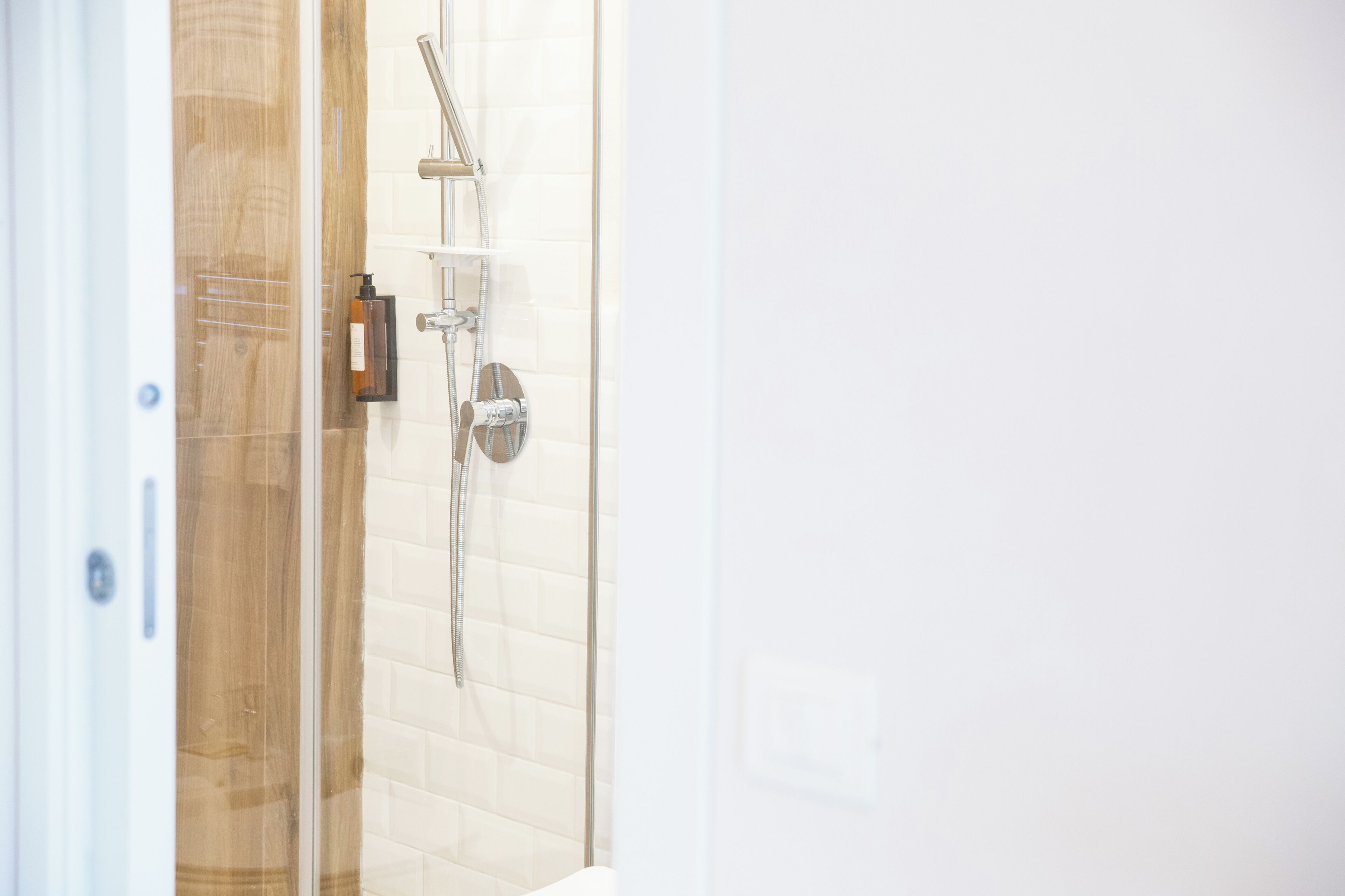 A glass-enclosed shower area with a handheld showerhead and a wall-mounted faucet.