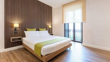 Una habitación de hotel moderna con una cama grande, un panel de pared de madera, dos lámparas de noche, una manta verde y un balcón con vistas.