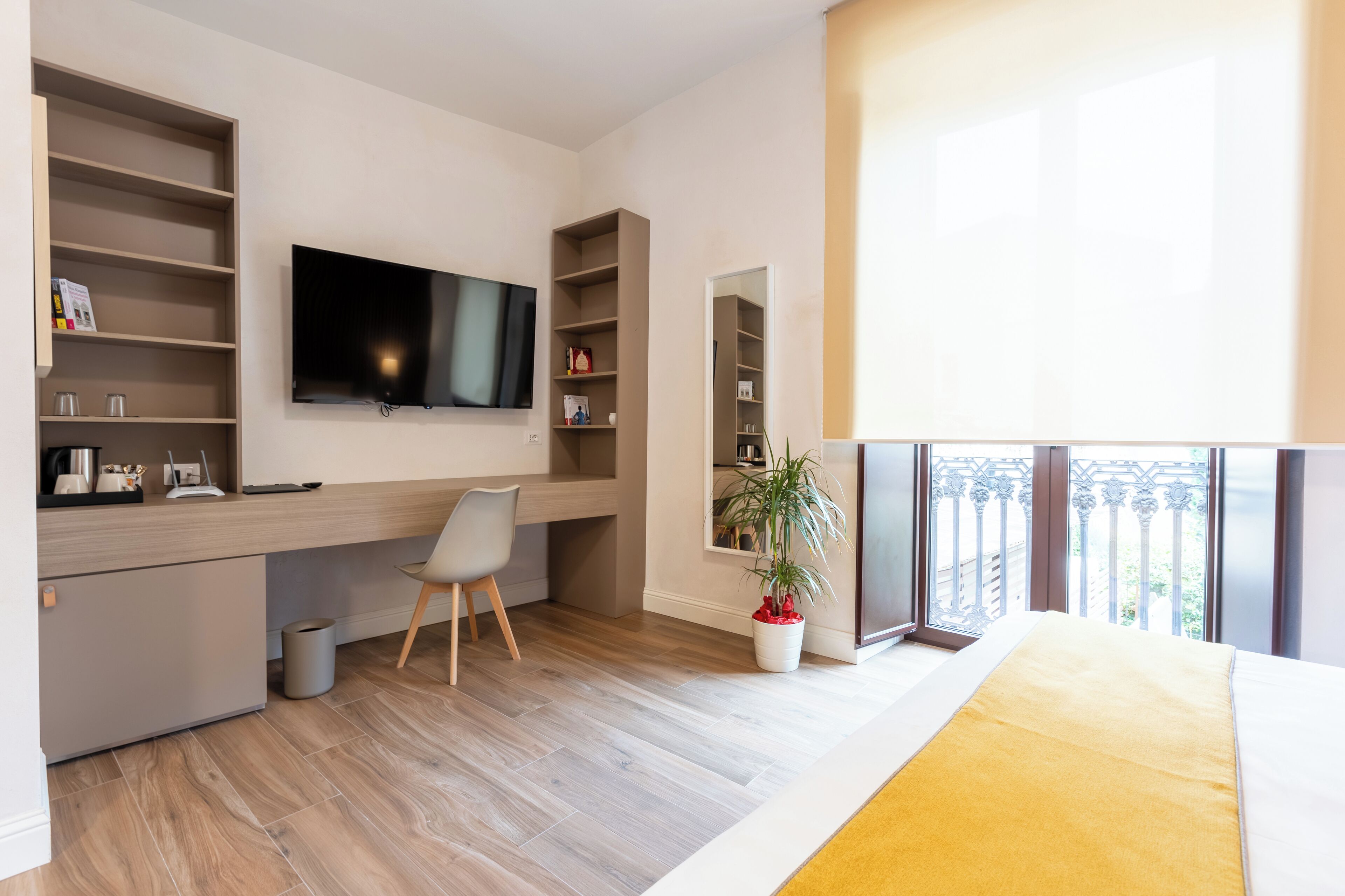 Ein modernes Schlafzimmer mit Bett, Schreibtisch, Fernseher und einem Balkon mit Geländer.