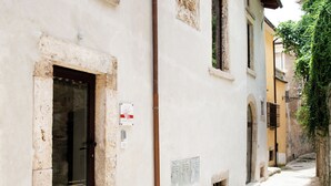 Una calle estrecha con un edificio de fachada de piedra, puerta de madera y una ventana pequeña.