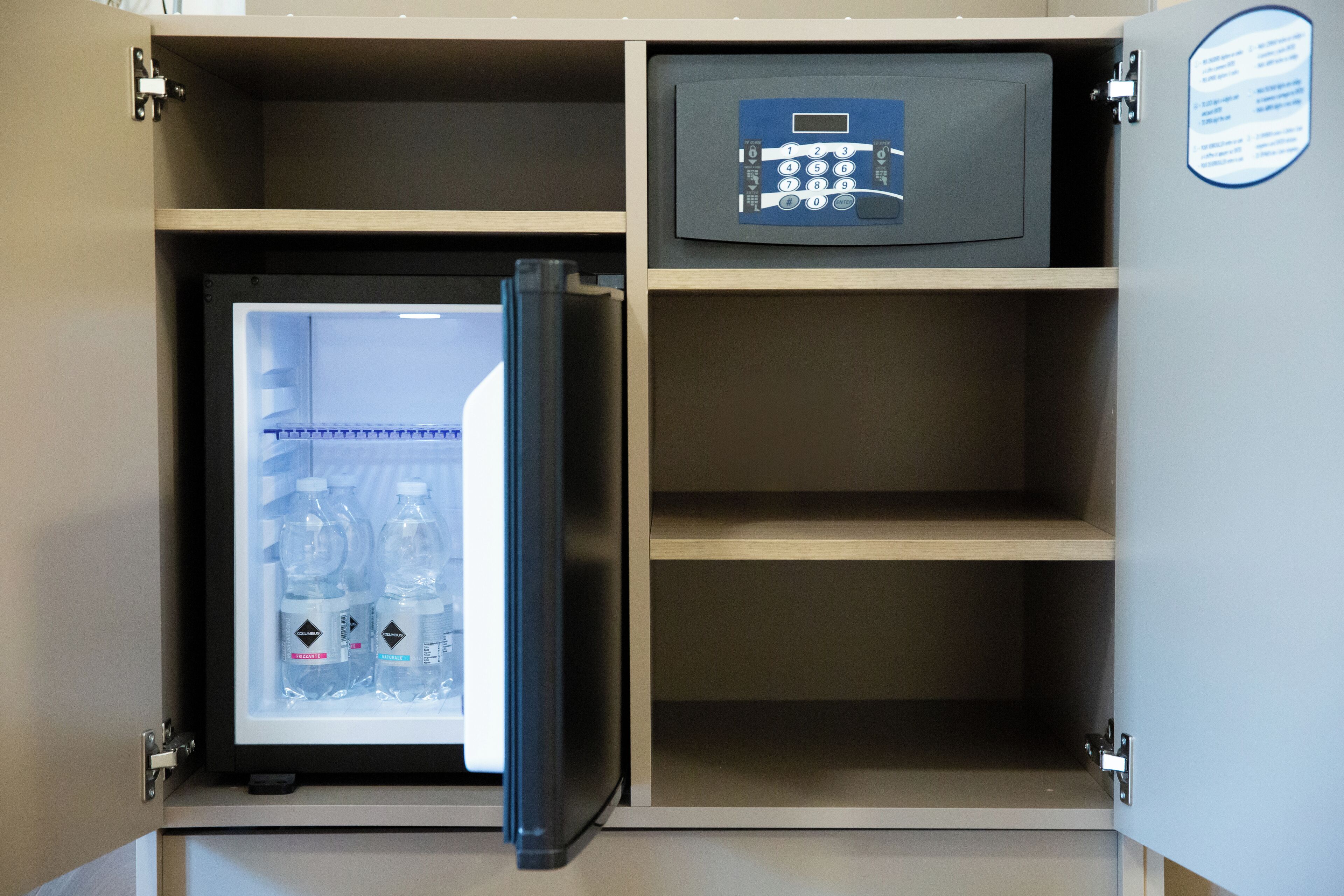 Un refrigerador compacto con congelador que contiene agua embotellada, un candado digital y un estante pequeño.