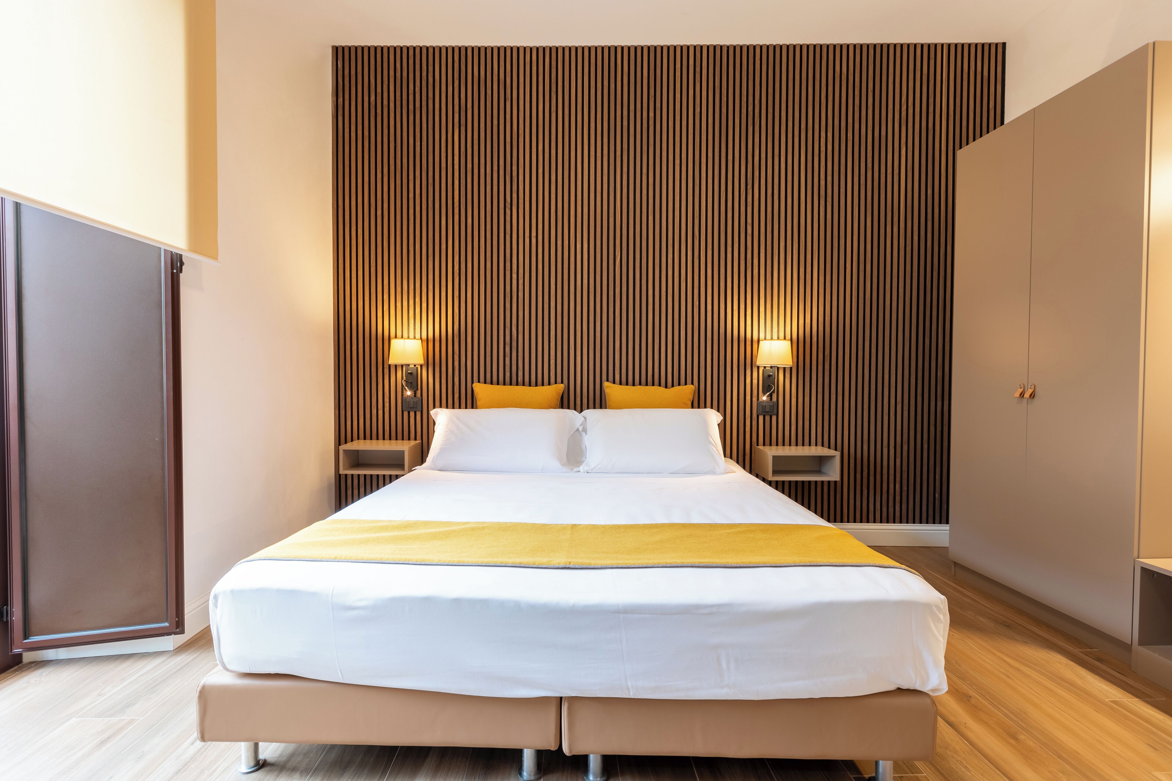 A modern hotel room with a large bed, wooden panel wall, and two bedside lamps.