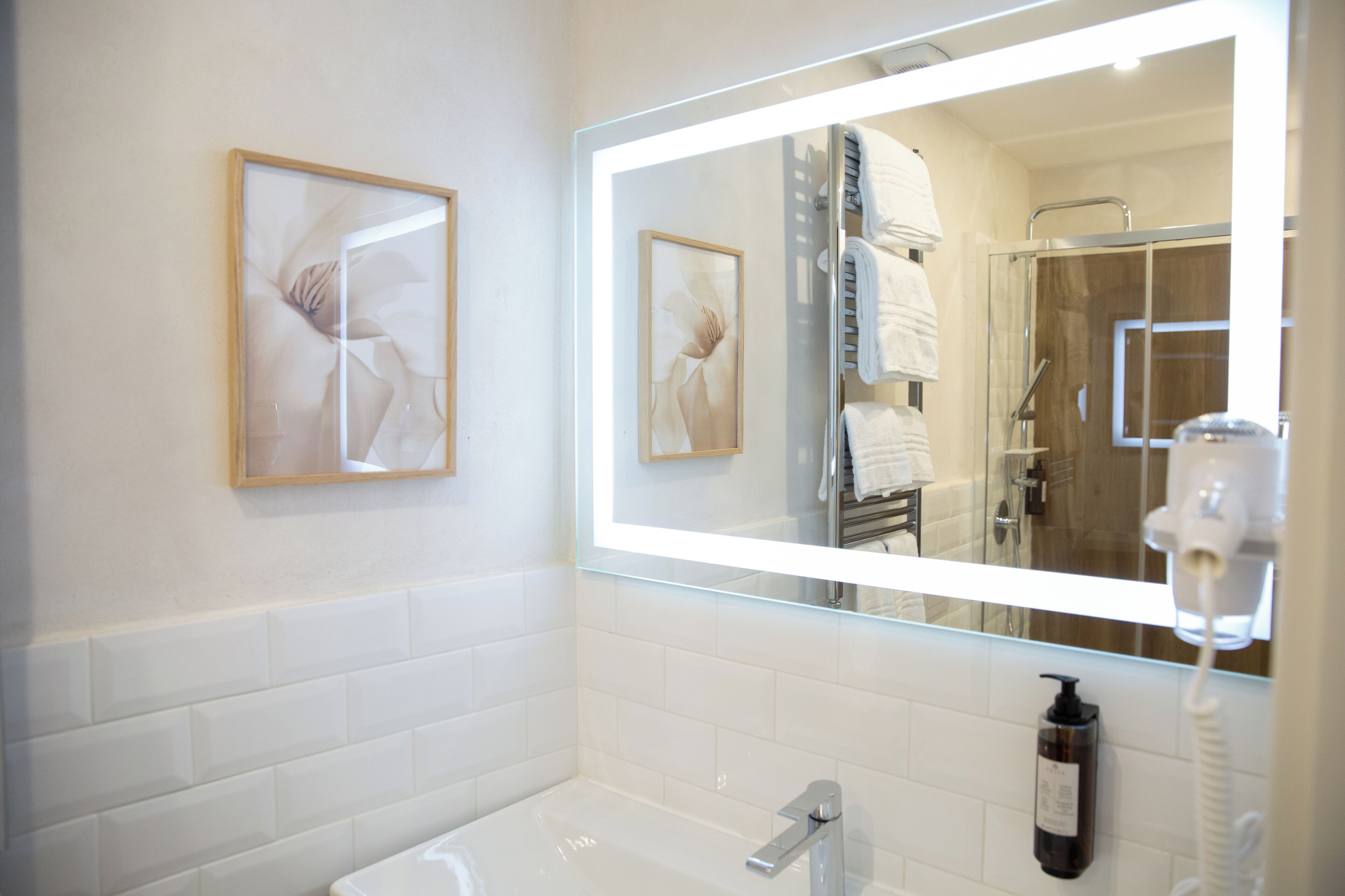 Un baño moderno con un espejo grande, azulejos blancos, una bañera y un secador de pelo.