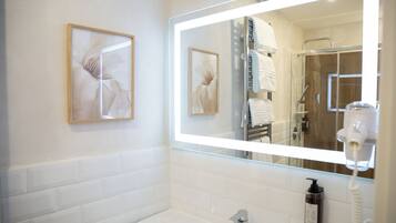 Un baño moderno con un espejo grande, azulejos blancos, una bañera y un secador de pelo.