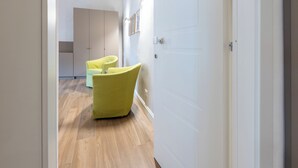 Un pasillo con suelo de madera, una silla amarilla y una puerta blanca.