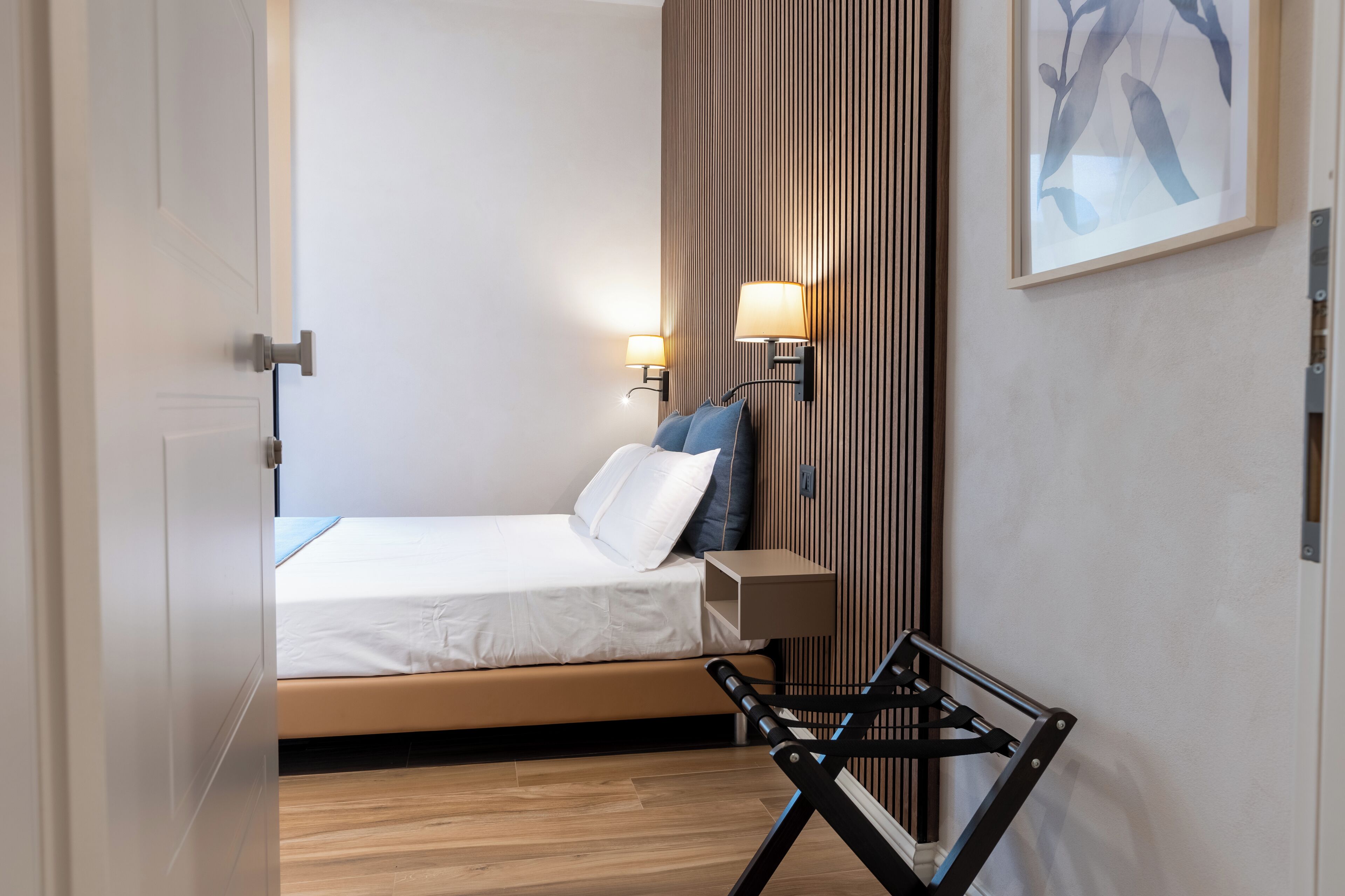 A modern bedroom with a bed, bedside lamps, a wall-mounted artwork, and a wooden floor.