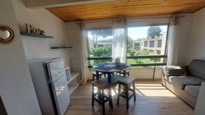 Eine kompakte Küche mit Kühlschrank, einem Esstisch mit Stühlen und einer Couch. Ein Fenster bietet Blick auf Gebäude und Grünflächen.