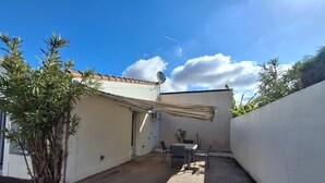 A small patio area with a table and chairs, surrounded by walls and plants.