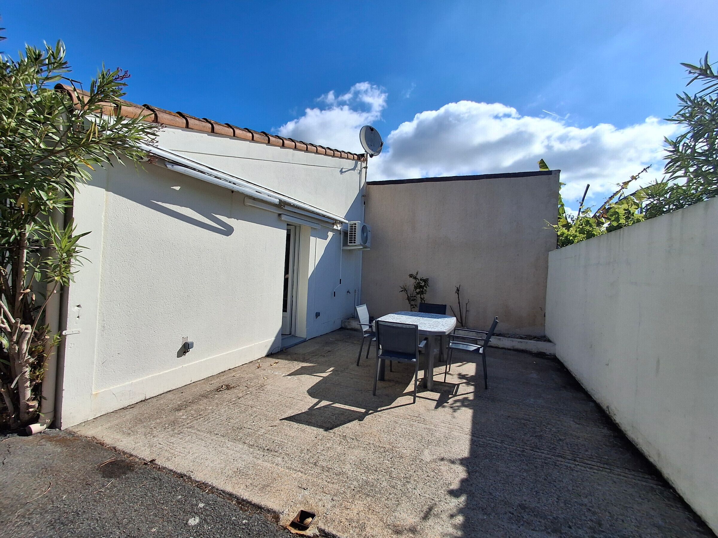 Une petite terrasse avec une table et des chaises, un mur blanc et une antenne parabolique.