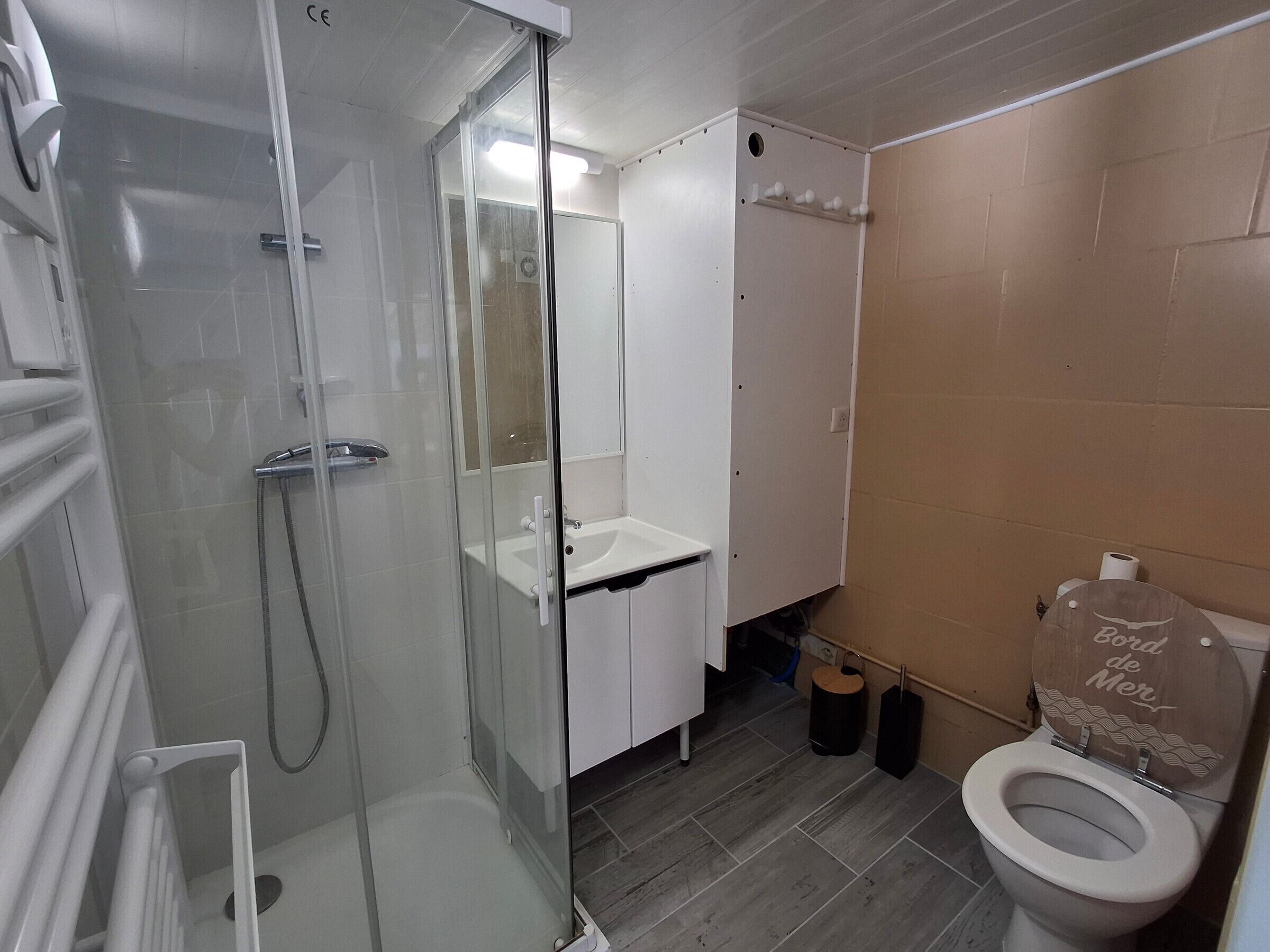 Une salle de bain dotée d’une douche à parois de verre, d’un lavabo blanc et de toilettes recouvertes d’un habillage décoratif.