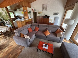 Ein modernes Wohnzimmer mit einer Eckcouch, einem kleinen Couchtisch und einer Küchenzeile im Hintergrund.