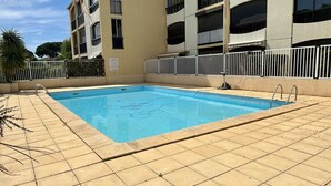 Piscina rectangular con borde empinado y solárium azulejado, rodeada por una cerca blanca.